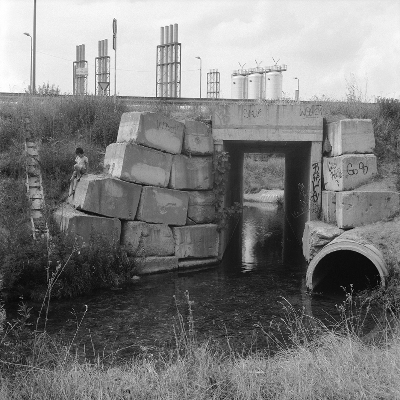 Un bambino in una pausa di gioco contempla le acque limpide della roggia Carlesca della periferia Sud. Milano, 2012